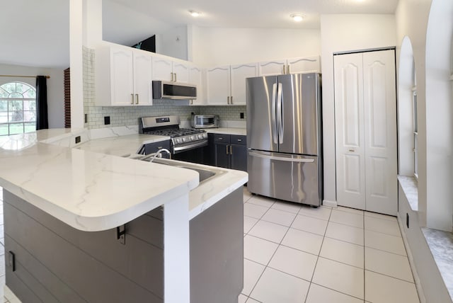 kitchen featuring lofted ceiling, kitchen peninsula, appliances with stainless steel finishes, white cabinetry, and a breakfast bar area