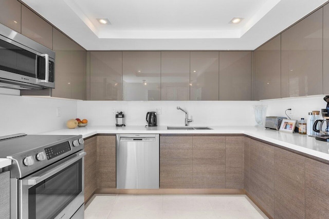 kitchen with stainless steel appliances, a tray ceiling, sink, and light tile patterned floors