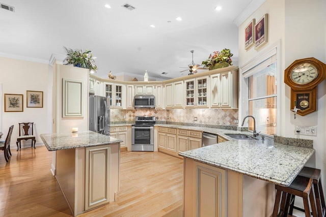 kitchen with light hardwood / wood-style floors, a breakfast bar, kitchen peninsula, stainless steel appliances, and sink