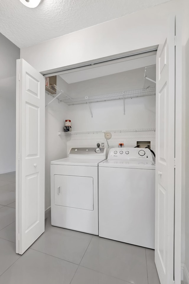 laundry area featuring a textured ceiling, light tile patterned floors, and washer and clothes dryer