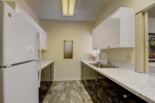 kitchen with white fridge, white cabinetry, sink, hardwood / wood-style flooring, and a textured ceiling