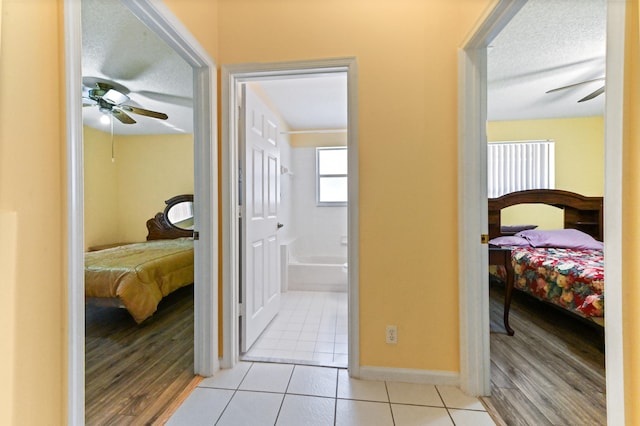 bedroom with ceiling fan, light hardwood / wood-style floors, a textured ceiling, and connected bathroom