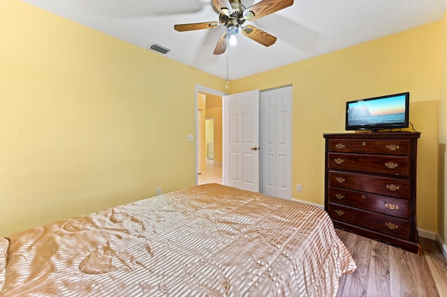 bedroom with ceiling fan, light hardwood / wood-style floors, a textured ceiling, and a closet