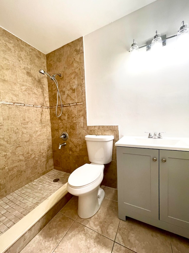 bathroom with a tile shower, tile patterned flooring, vanity, and toilet