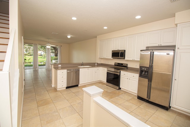 kitchen featuring kitchen peninsula, stainless steel appliances, sink, light tile patterned floors, and white cabinetry