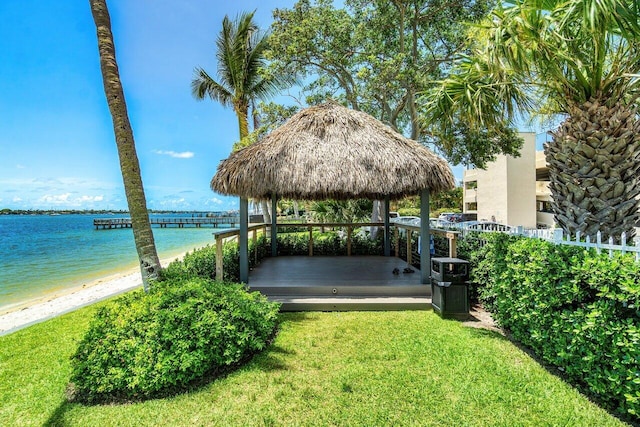 dock area with a gazebo, a lawn, a water view, and a view of the beach