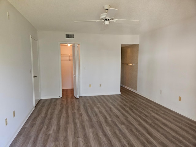 unfurnished bedroom with a closet, a textured ceiling, a walk in closet, dark hardwood / wood-style flooring, and ceiling fan