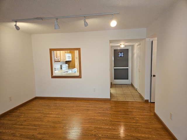 spare room featuring a textured ceiling, light hardwood / wood-style floors, and track lighting