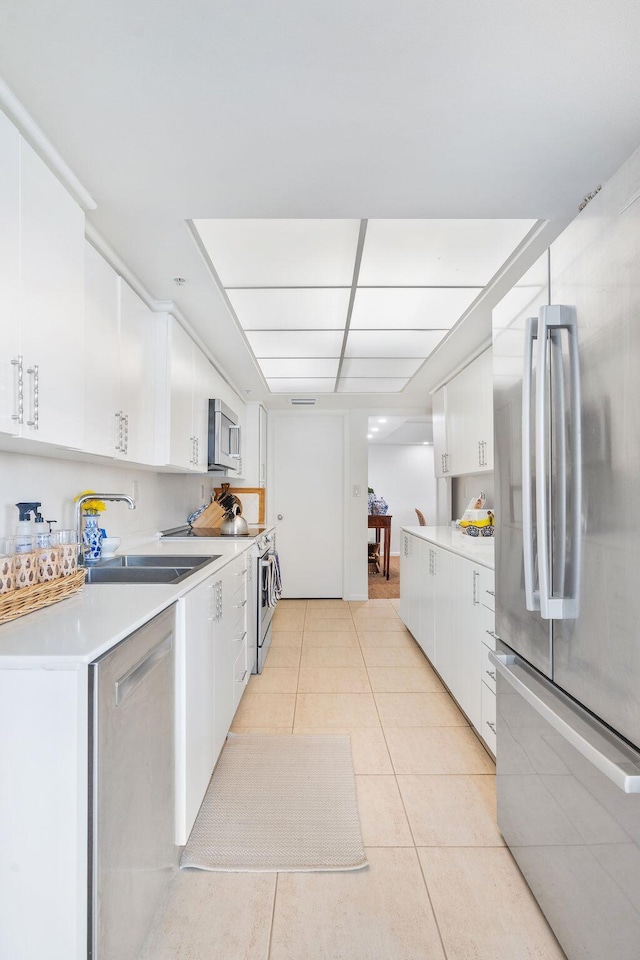 kitchen with sink, light tile patterned floors, stainless steel appliances, and white cabinets