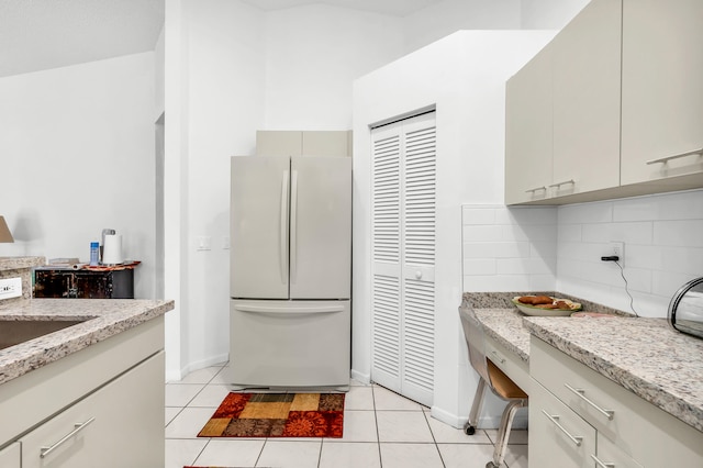 kitchen featuring decorative backsplash, light stone countertops, light tile patterned flooring, and white fridge