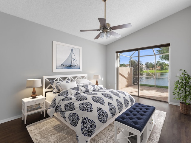 bedroom featuring access to exterior, dark hardwood / wood-style flooring, a water view, lofted ceiling, and ceiling fan