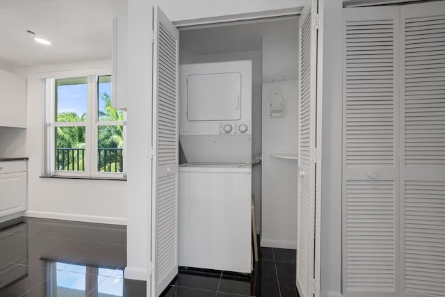 laundry area featuring stacked washer and clothes dryer and dark tile patterned floors