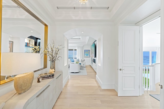 hallway featuring light hardwood / wood-style floors, ornamental molding, a tray ceiling, and a water view