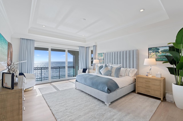 bedroom with light hardwood / wood-style flooring, a water view, access to outside, and a raised ceiling