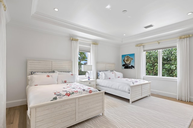 bedroom with a raised ceiling, ornamental molding, and light wood-type flooring