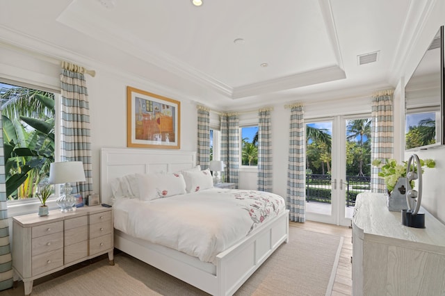 bedroom with access to exterior, a tray ceiling, light hardwood / wood-style flooring, ornamental molding, and french doors