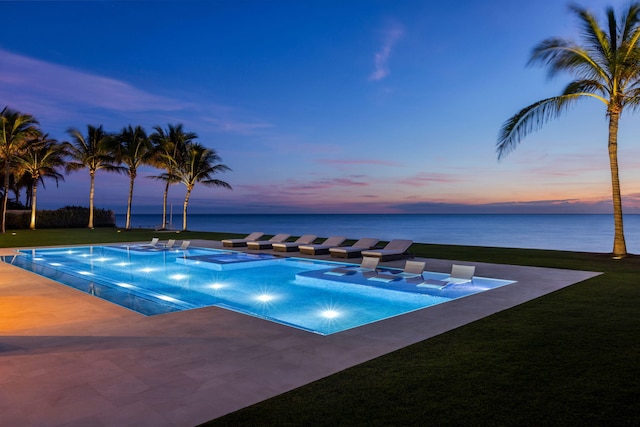 pool at dusk featuring a water view and a lawn