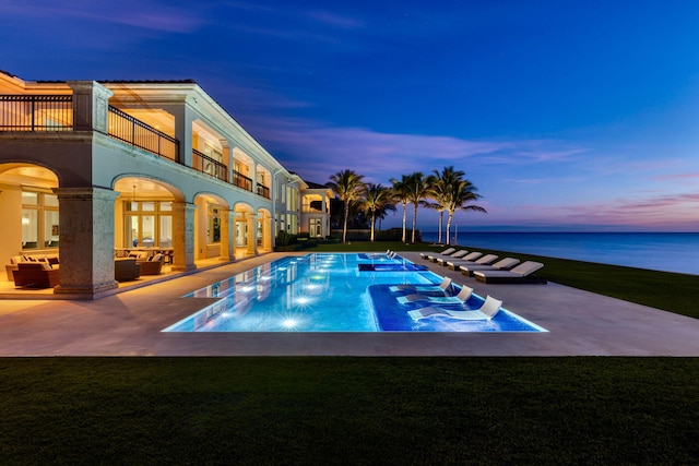 pool at dusk featuring a patio, a lawn, and a water view