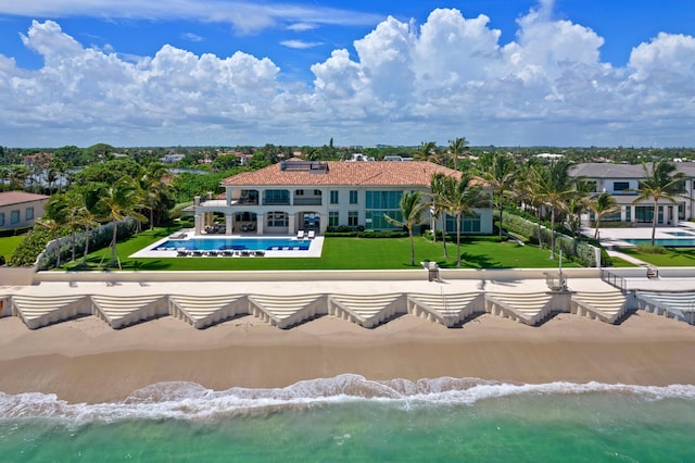 rear view of property featuring a swimming pool, a water view, a lawn, and a view of the beach