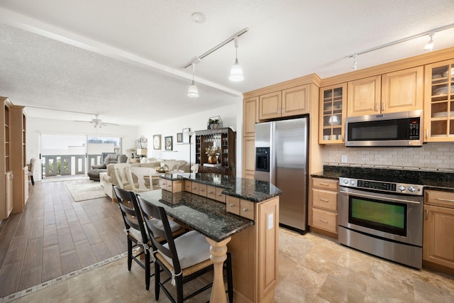 kitchen featuring light hardwood / wood-style floors, dark stone counters, decorative light fixtures, appliances with stainless steel finishes, and a kitchen bar