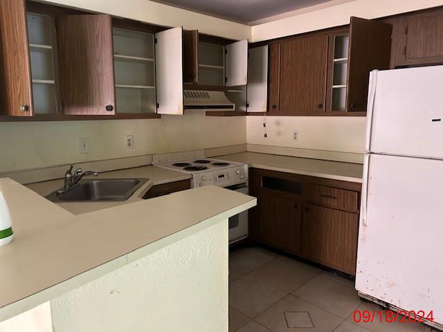 kitchen with dark brown cabinetry, white appliances, sink, and dark tile patterned flooring