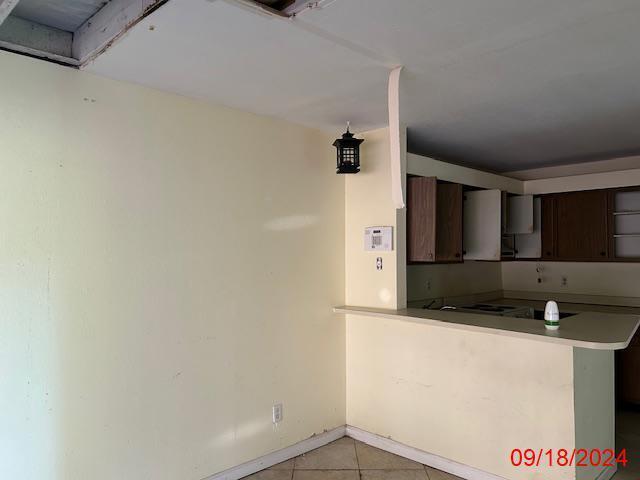 kitchen with light tile patterned floors, kitchen peninsula, dark brown cabinets, and extractor fan