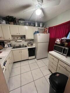 kitchen featuring sink, a textured ceiling, ceiling fan, white fridge, and light tile patterned floors