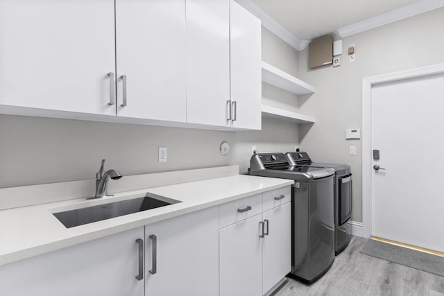 laundry room featuring cabinets, washer and clothes dryer, crown molding, sink, and light hardwood / wood-style flooring