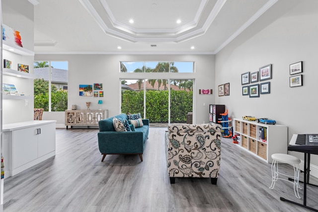 living room featuring light wood-type flooring, a raised ceiling, a wealth of natural light, and crown molding