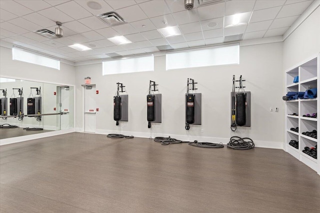 gym with a paneled ceiling, visible vents, baseboards, and wood finished floors