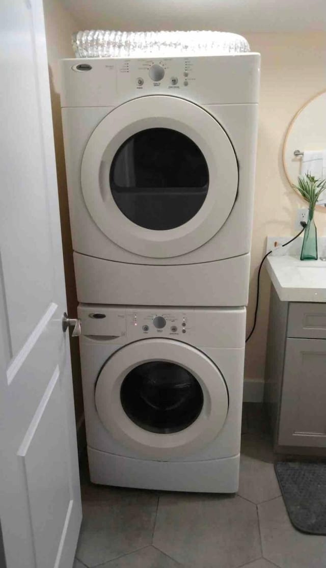 laundry area featuring stacked washing maching and dryer, light tile patterned floors, and cabinets