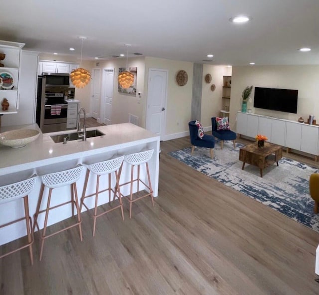 kitchen featuring decorative light fixtures, white cabinets, appliances with stainless steel finishes, a kitchen bar, and hardwood / wood-style flooring