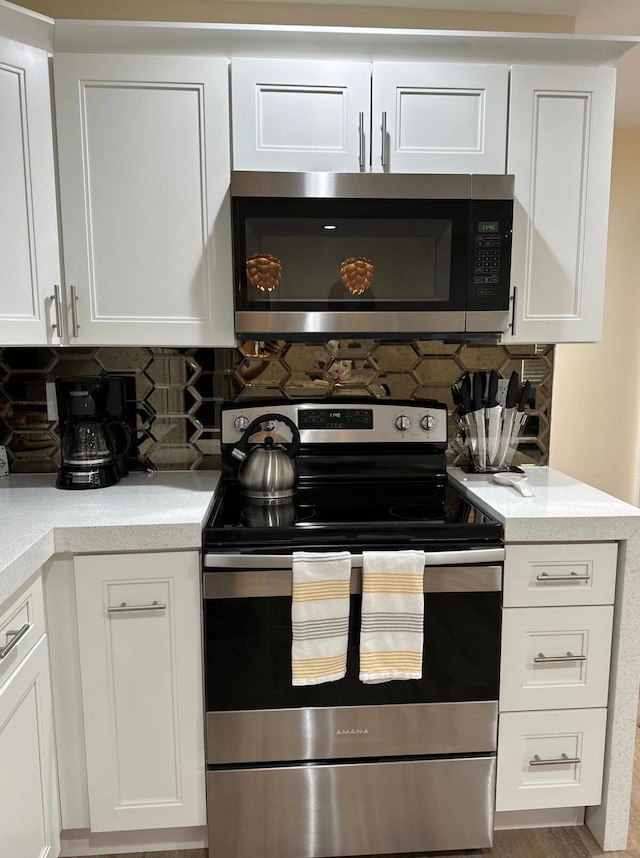 kitchen with white cabinets, appliances with stainless steel finishes, hardwood / wood-style floors, and tasteful backsplash