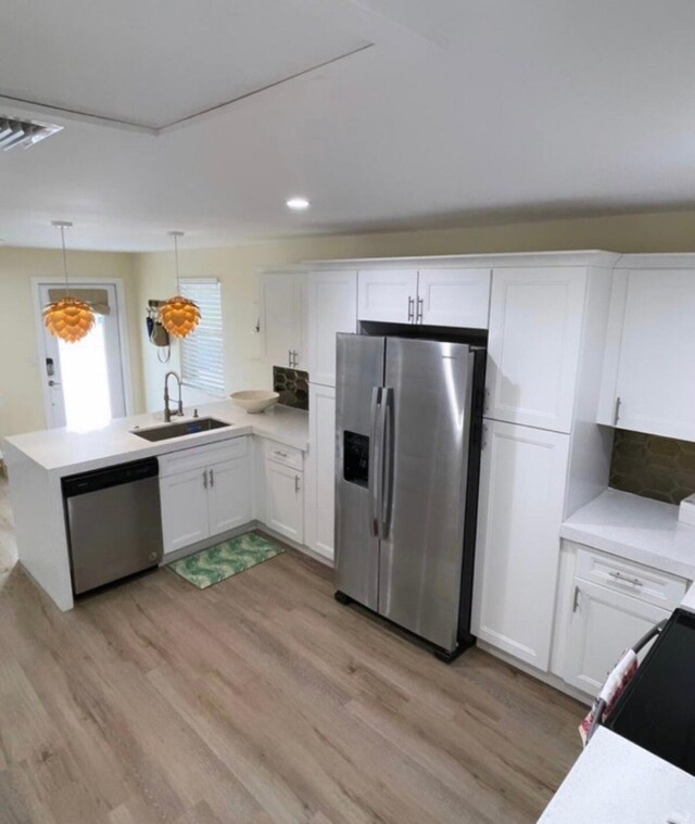 kitchen with white cabinets, sink, kitchen peninsula, appliances with stainless steel finishes, and decorative light fixtures