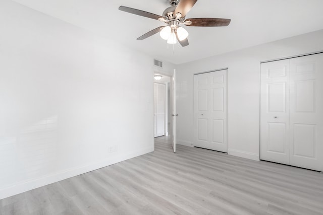 unfurnished bedroom featuring ceiling fan, multiple closets, and light hardwood / wood-style flooring