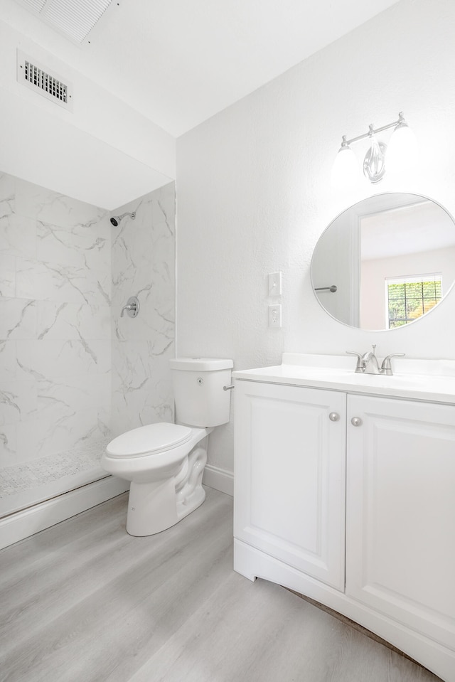 bathroom featuring vanity, hardwood / wood-style floors, toilet, and tiled shower