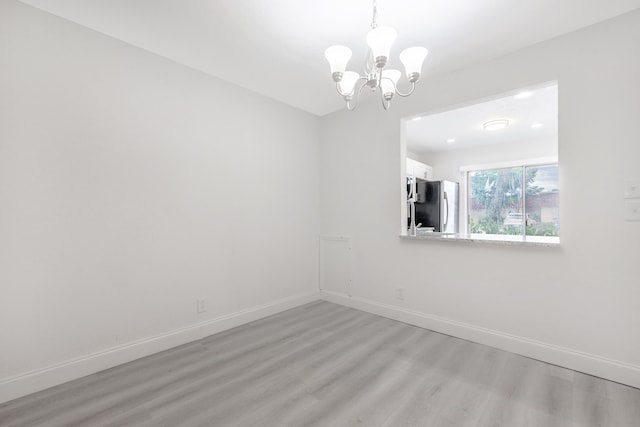 spare room with light hardwood / wood-style floors and a chandelier