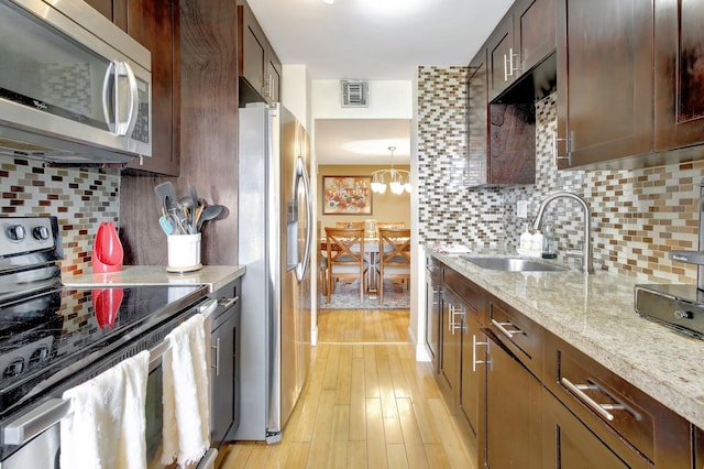 kitchen with light stone counters, sink, light hardwood / wood-style floors, appliances with stainless steel finishes, and backsplash