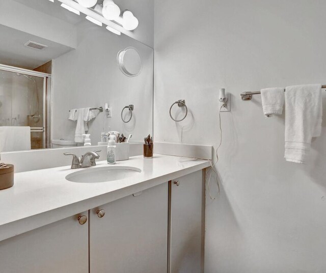 bathroom with toilet, vanity, and a shower with shower door