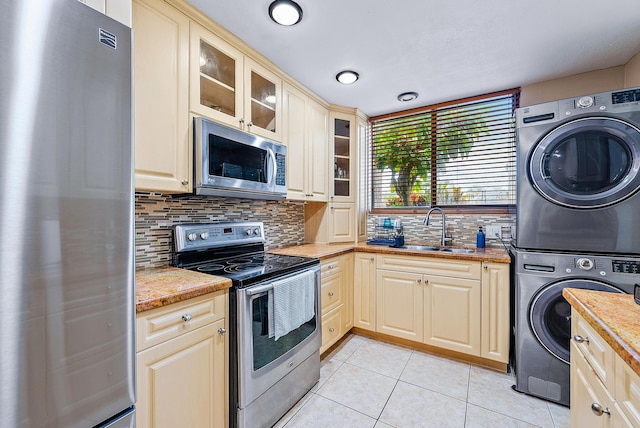 kitchen featuring stainless steel appliances, tasteful backsplash, sink, light tile patterned flooring, and stacked washer / drying machine