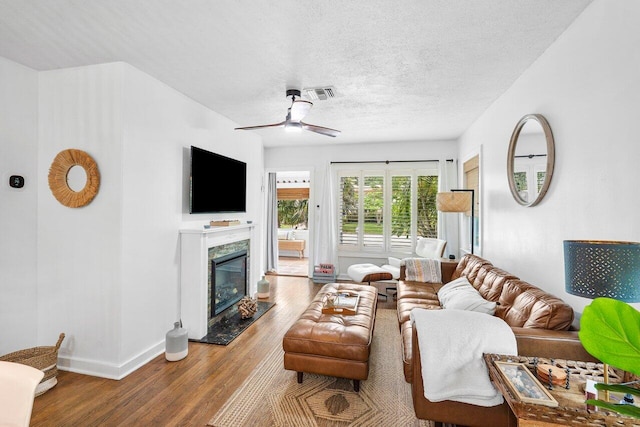 living room with a high end fireplace, wood-type flooring, a textured ceiling, and ceiling fan