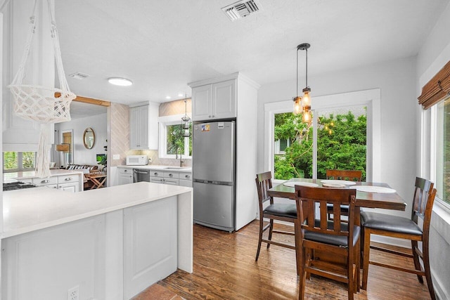 kitchen featuring white cabinetry, dark hardwood / wood-style flooring, kitchen peninsula, decorative light fixtures, and appliances with stainless steel finishes