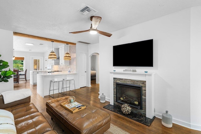 living room with a stone fireplace, ceiling fan, dark hardwood / wood-style floors, and a textured ceiling