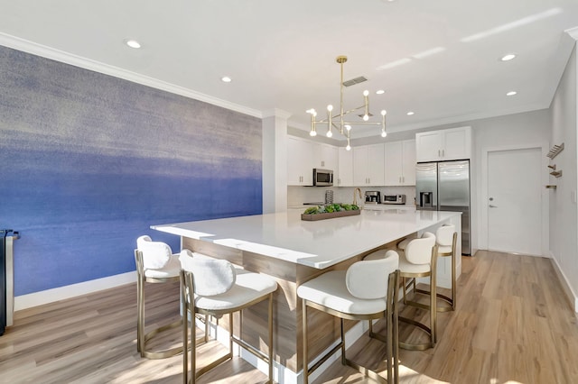 kitchen with appliances with stainless steel finishes, light hardwood / wood-style floors, decorative light fixtures, white cabinets, and ornamental molding