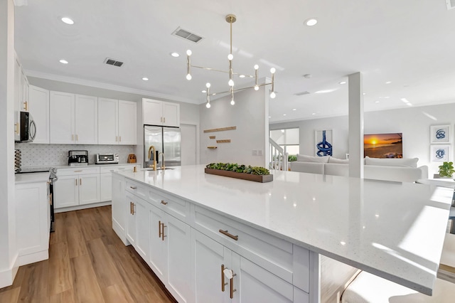 kitchen with appliances with stainless steel finishes, white cabinetry, light stone countertops, light hardwood / wood-style flooring, and crown molding