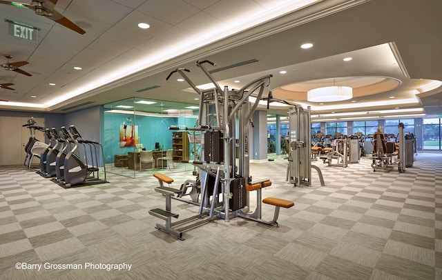 gym featuring ornamental molding, light colored carpet, a tray ceiling, and ceiling fan