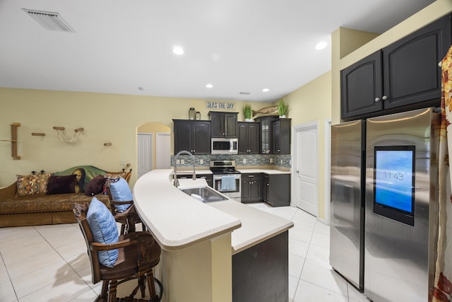 kitchen with stainless steel appliances, tasteful backsplash, an island with sink, a breakfast bar area, and light tile patterned floors