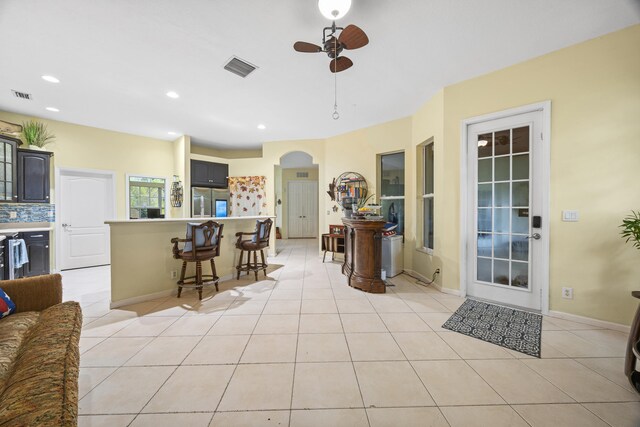 kitchen featuring decorative backsplash, stainless steel fridge, ceiling fan, light tile patterned floors, and a breakfast bar area