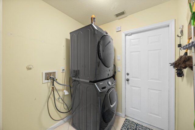 washroom with stacked washer and dryer and light tile patterned floors