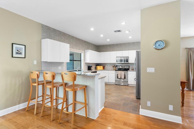 kitchen featuring light hardwood / wood-style flooring, white cabinets, stainless steel appliances, and kitchen peninsula